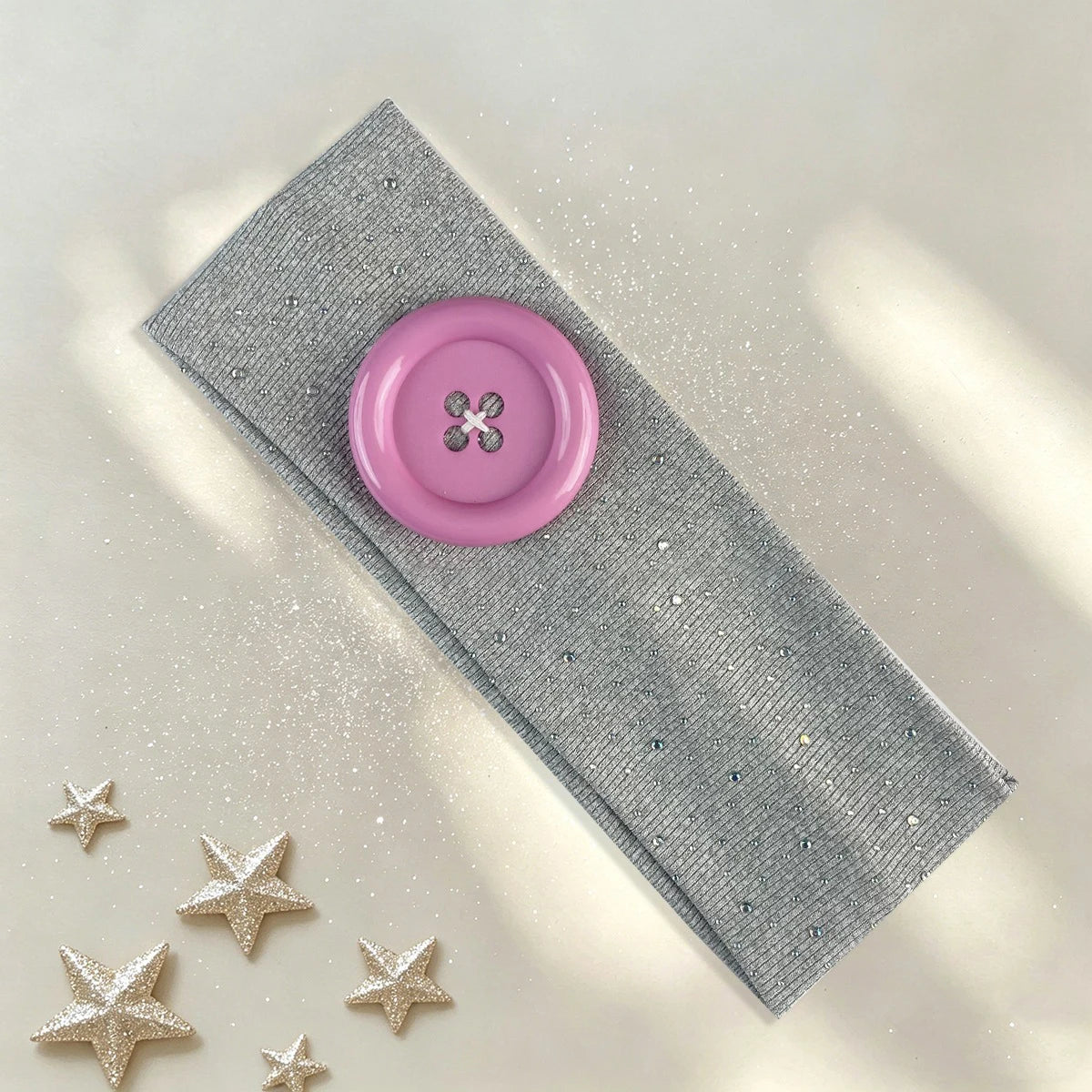 A pink vintage polka dot button headband resting on a light surface with silver glitter stars.