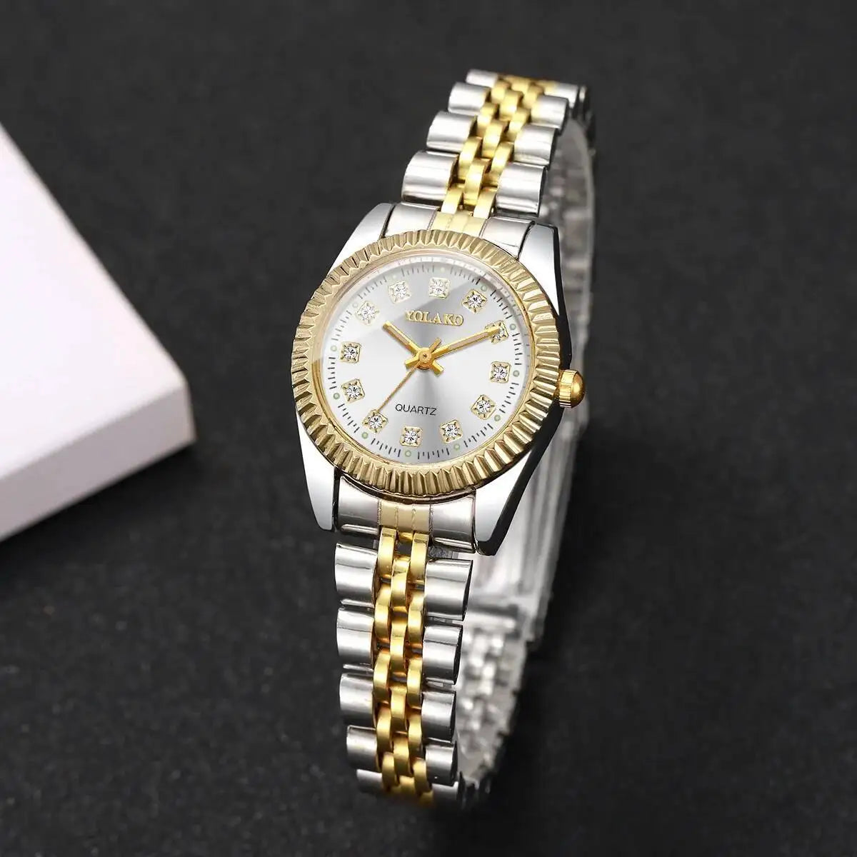 A silver and gold rhinestone quartz wristwatch with a metal bracelet is shown on a dark background.
