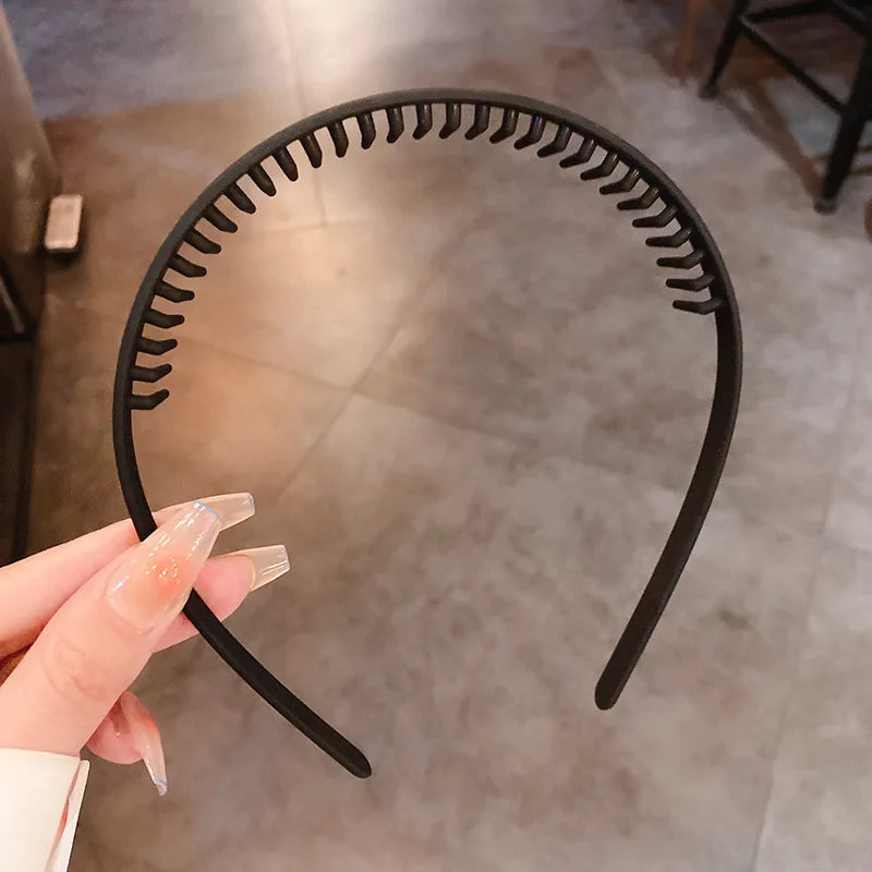 A close-up of a black resin wave toothed headband being held by a hand against a neutral background.