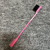 Pinkes, zweischneidiges Augenbrauenkamm mit schwarzen Borsten auf grauer, strukturierter Oberfläche.