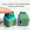 A green frog light-up keychain with a sound-emitting design resting on a marble surface.