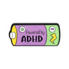 An enamel lapel pin featuring a purple background with the text Powered by ADHD and yellow and green lightning bolt symbols.