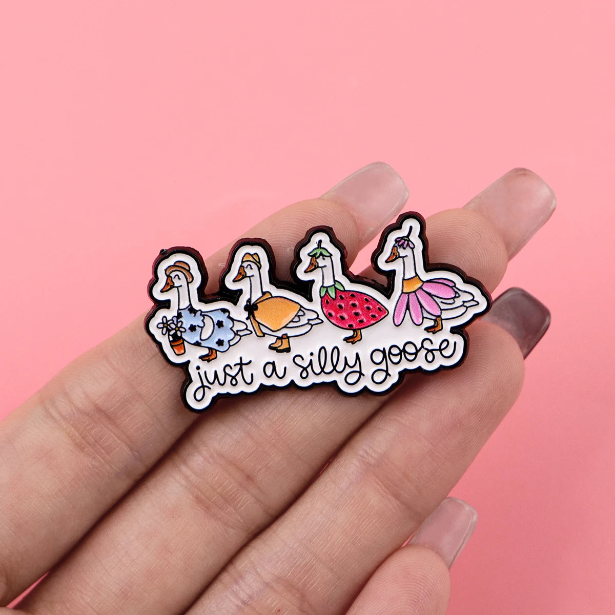 A hand holds a set of black enamel pins depicting a silly goose character.