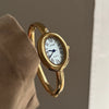 A hand holds a gold Zidoo quartz analog watch with an oval face, showing the watch's side profile.