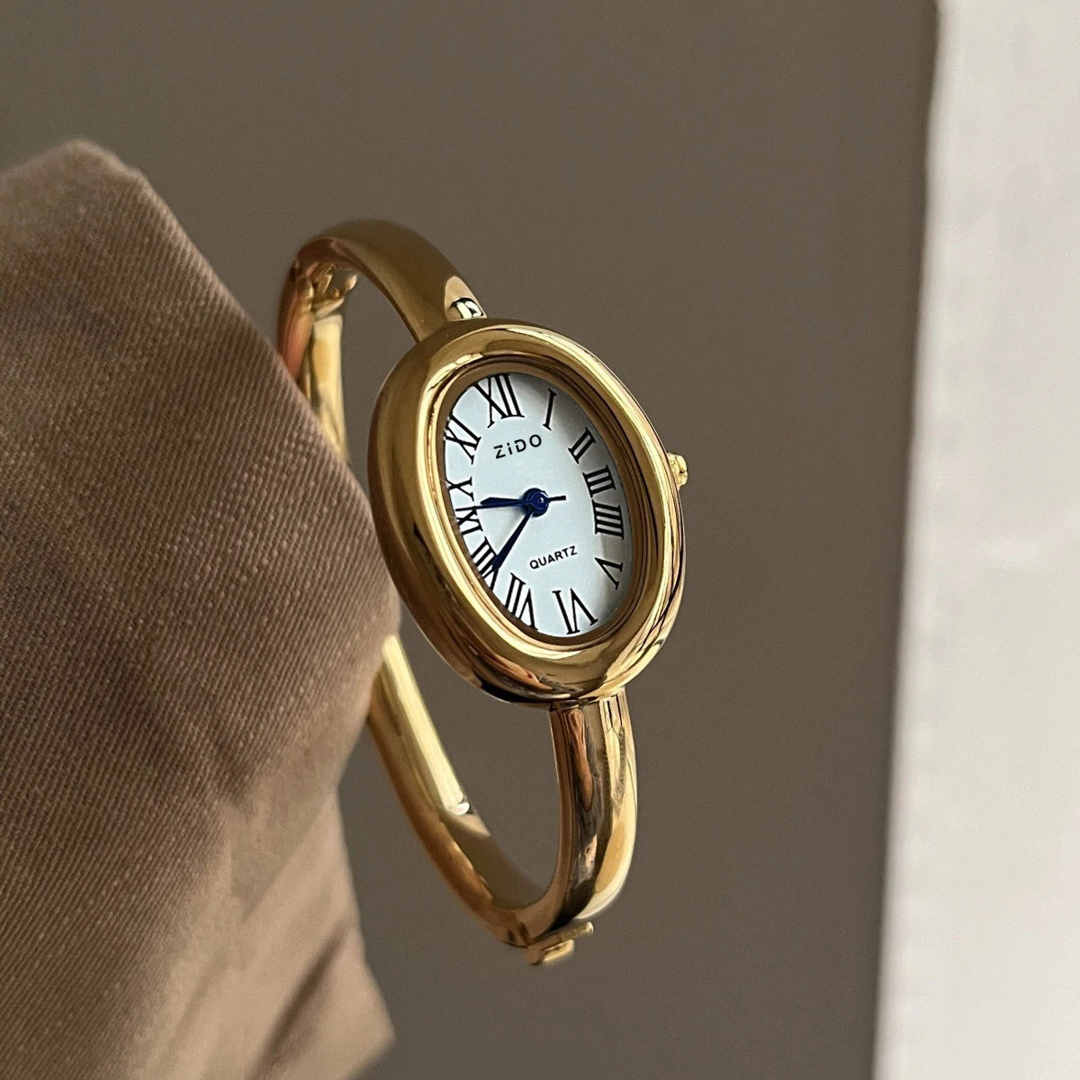 A hand holds a gold Zidoo quartz analog watch with an oval face, showing the watch's side profile.