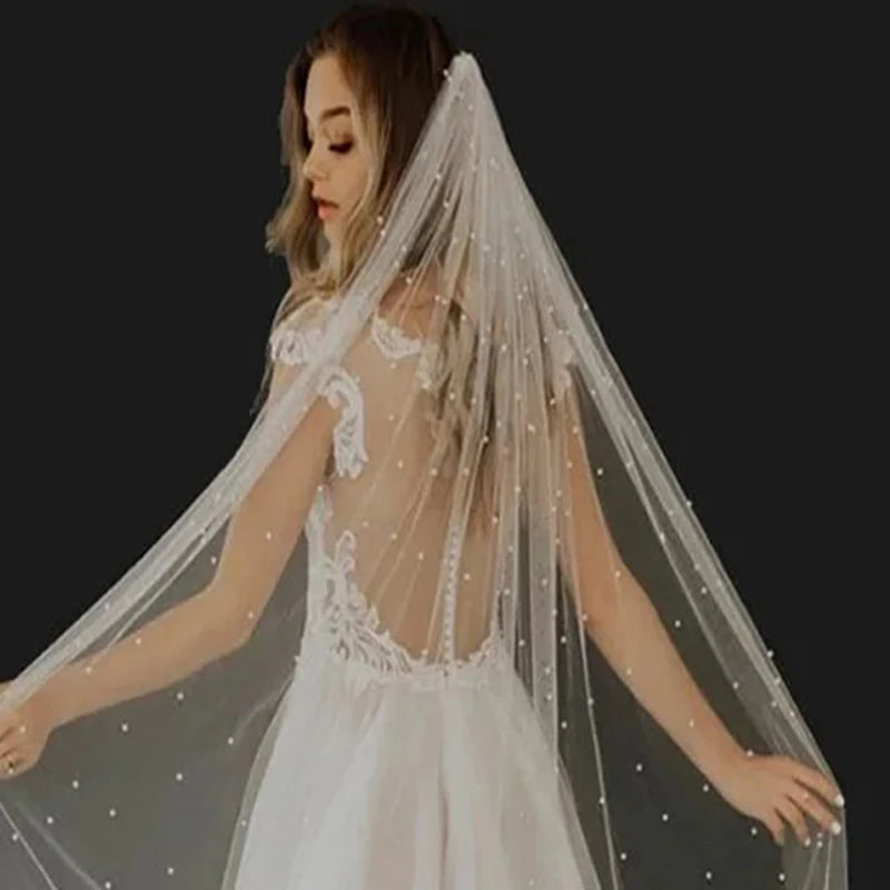 Una novia vistiendo un velo de perlas y un vestido con bordados, vista desde atrás.
