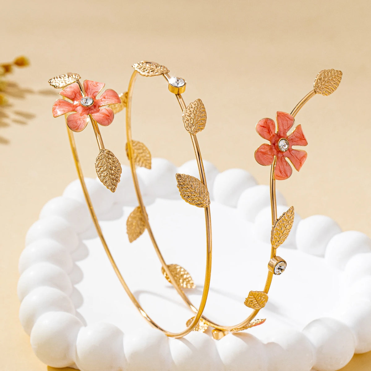 Gold floral vine arm bracelet with pink flowers and gold leaves displayed on a white surface