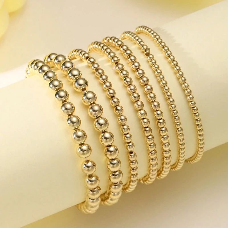 A set of gold and silver round beaded bracelets stacked on a white surface.