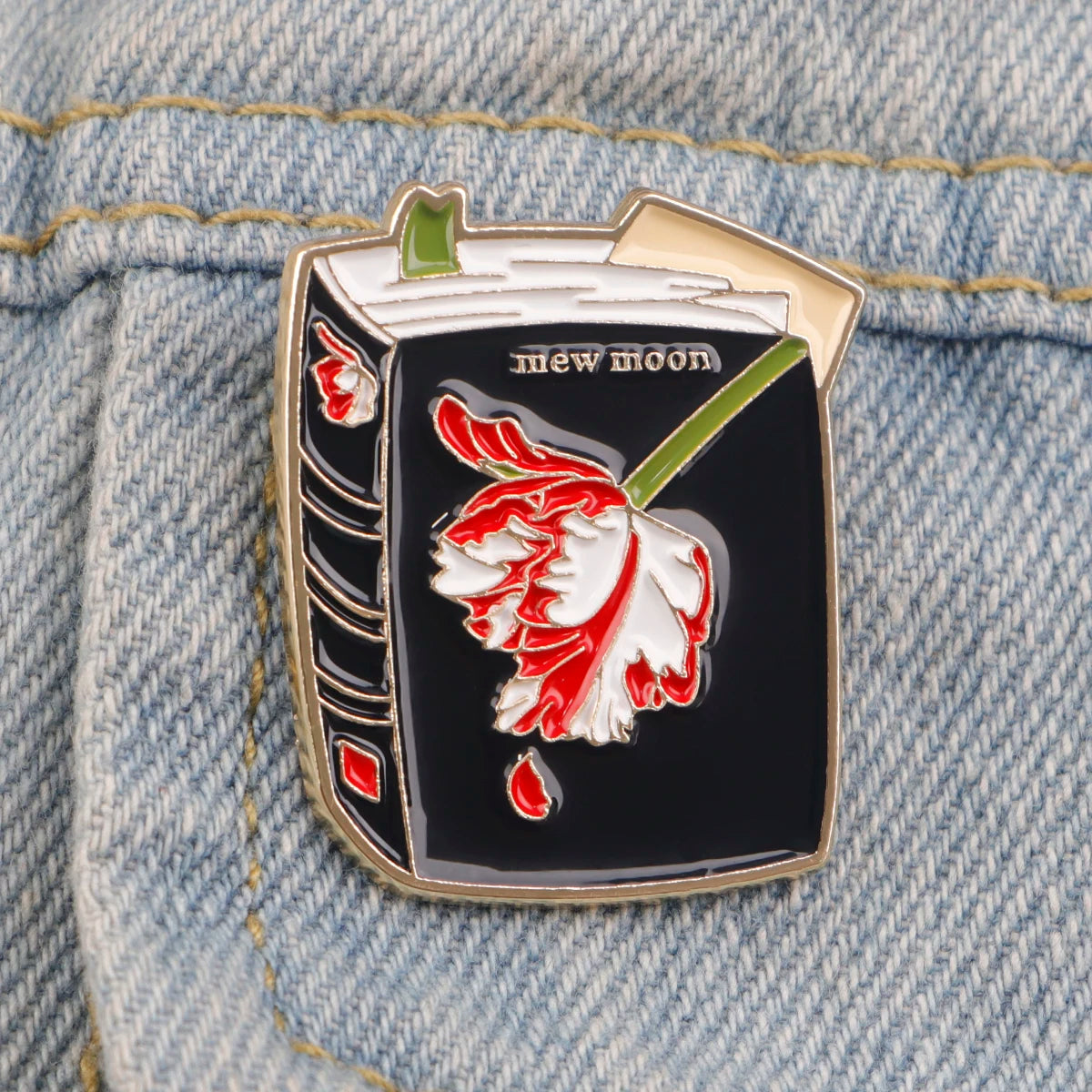 Broche en émail argentée en forme de poisson avec une rose rouge et une tige verte sur fond de denim.