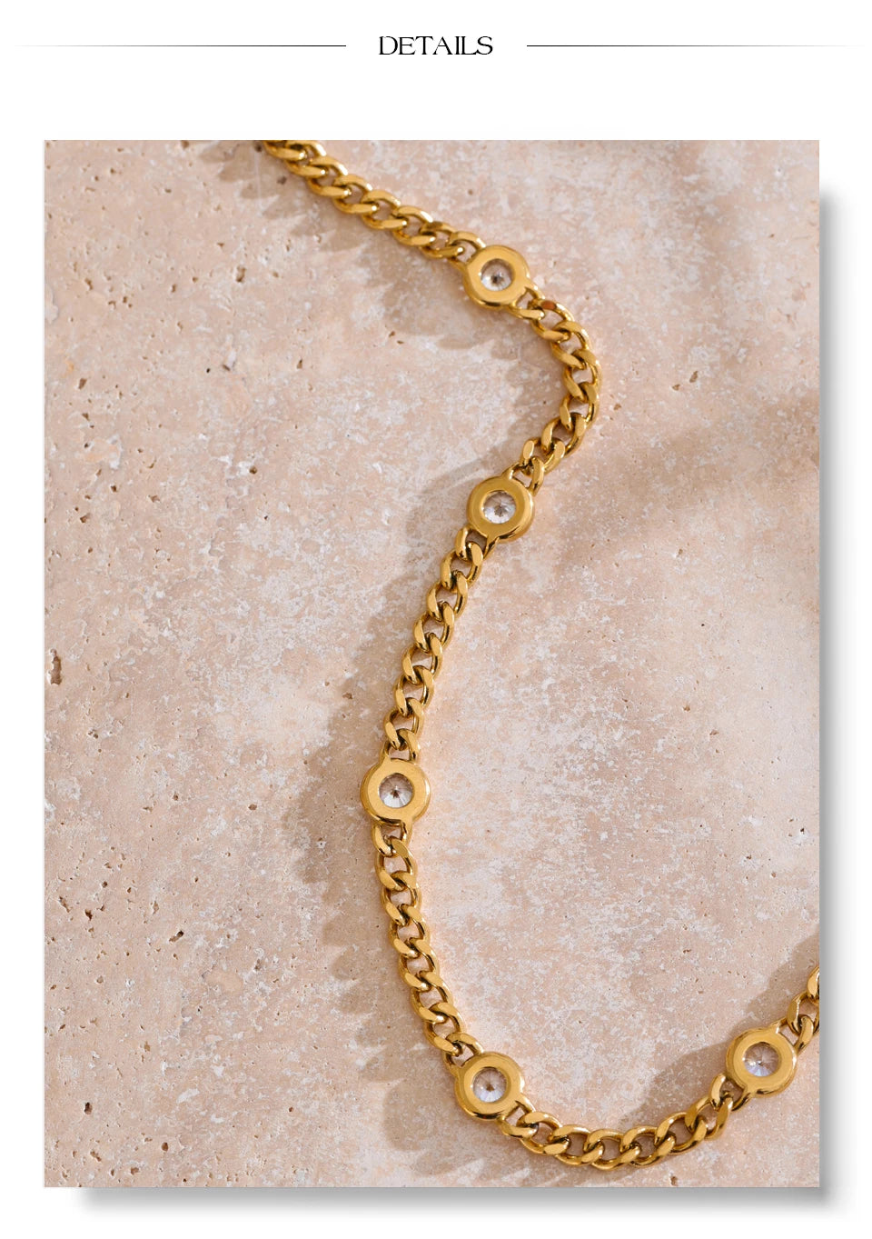 A close-up of a gold-toned chain necklace featuring clear CZ charms resting on a light pink marble surface.