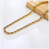 A delicate gold rope chain necklace laid across a light brown textured surface.