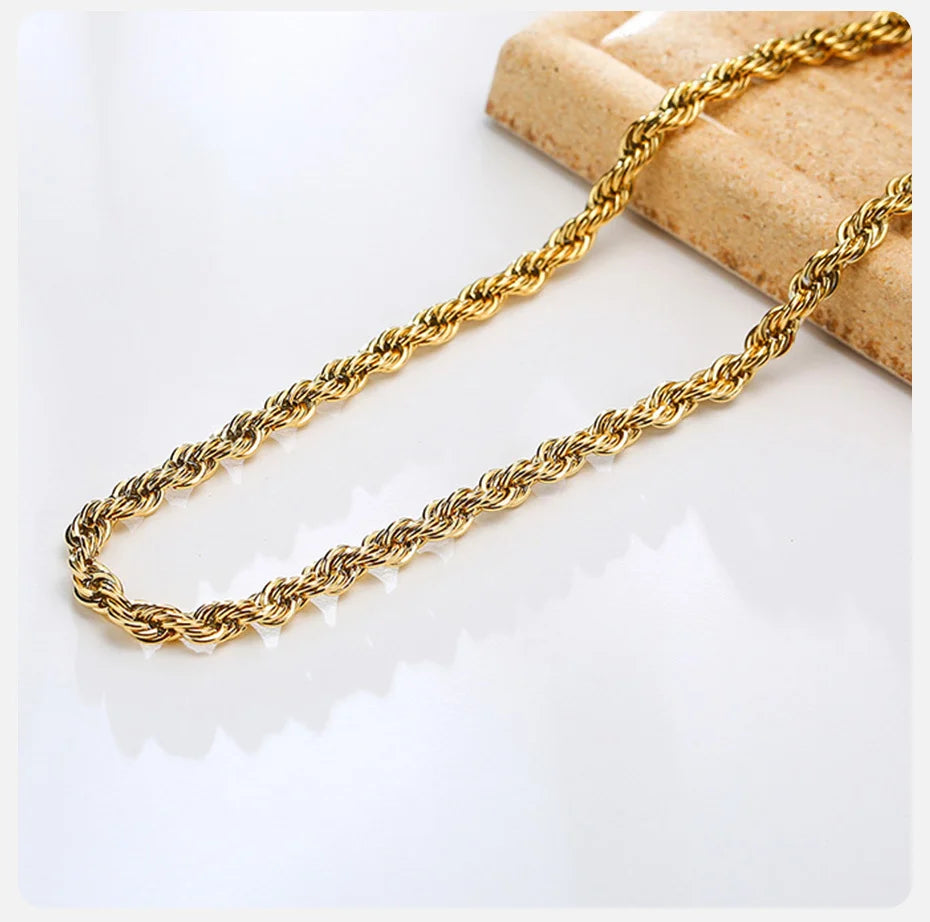 A delicate gold rope chain necklace laid across a light brown textured surface.