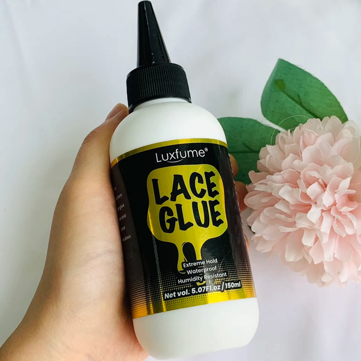 Eine Hand hält eine Flasche Lace Glue, eine klare Flüssigkeit in einer weißen Flasche mit schwarzem Deckel und gelber Etikett