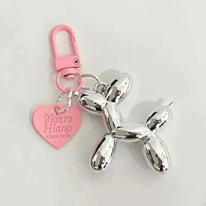 A silver cartoon dog keychain with a heart-shaped pink charm and a pink keyring.