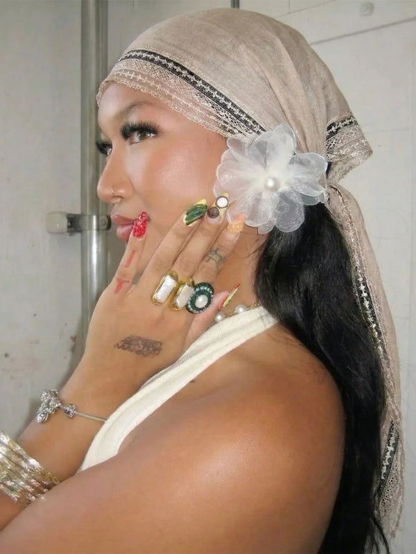 A woman wearing a beige bohemian lace trim shawl scarf and jewelry, looking to the side.