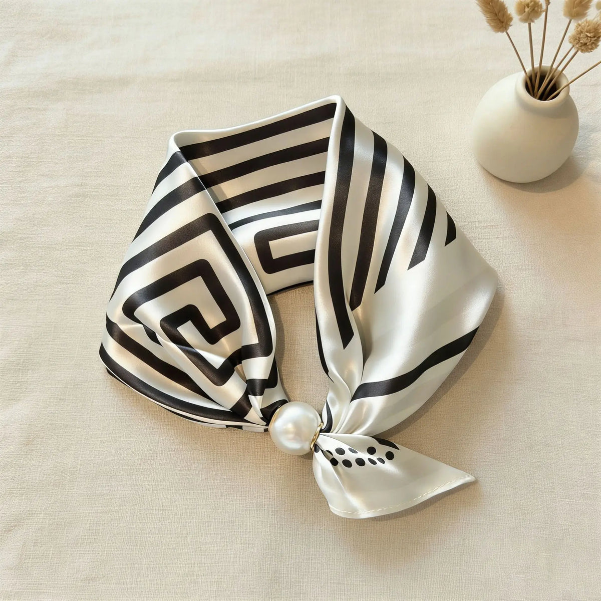 A silk scarf featuring a black and white maze pattern tied in a bow, resting on a light beige fabric.