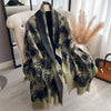 A draped olive green and black patterned cashmere scarf or shawl displayed on a white chair.