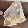 A sheer silk scarf with a gold and silver floral print draped over a brown leather sofa.