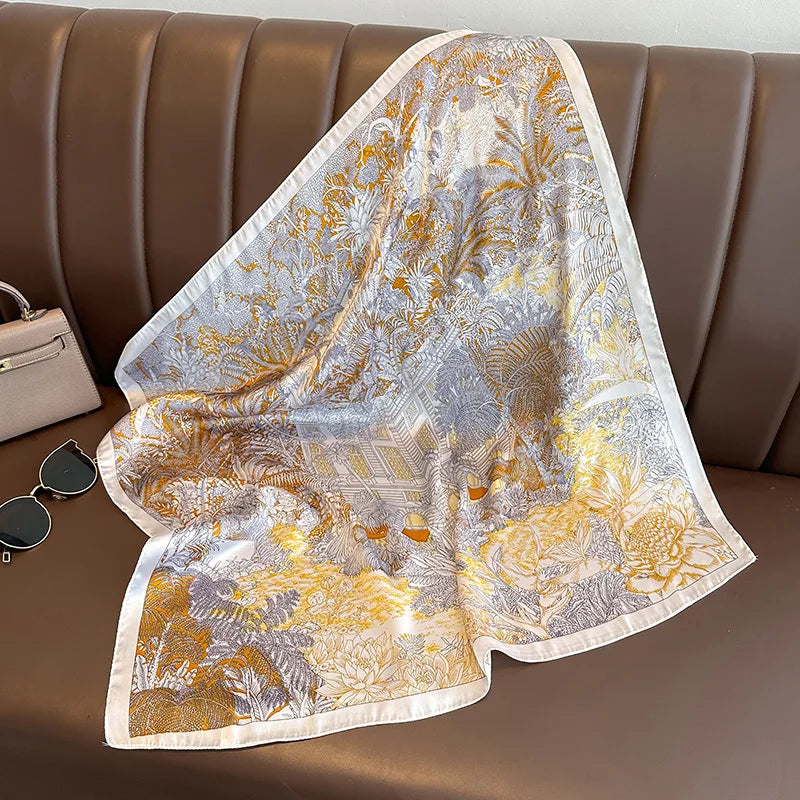 A sheer silk scarf with a gold and silver floral print draped over a brown leather sofa.