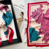 A pink floral print silk scarf draped in a black frame, featuring vibrant pink and teal hues.