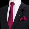 Chaqueta oscura con camisa blanca, corbata de seda marrón rojiza y un prendido floral rojo oscuro en la solapa.