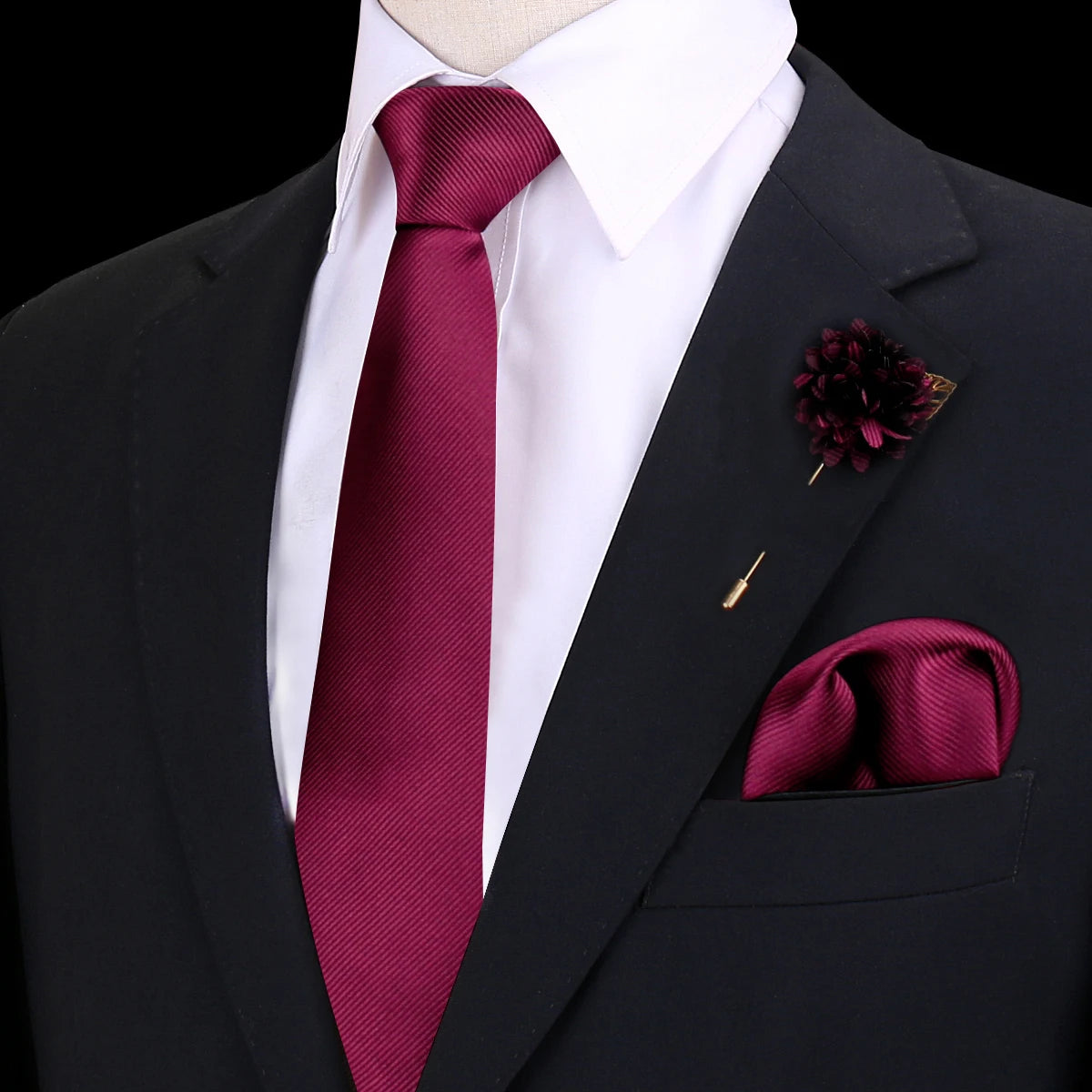 Chaqueta oscura con camisa blanca, corbata de seda marrón rojiza y un prendido floral rojo oscuro en la solapa.