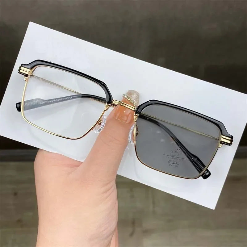 Eine Hand hält eine goldgerahmte photochromische Brille mit dunklen Gläsern vor weißem Hintergrund.