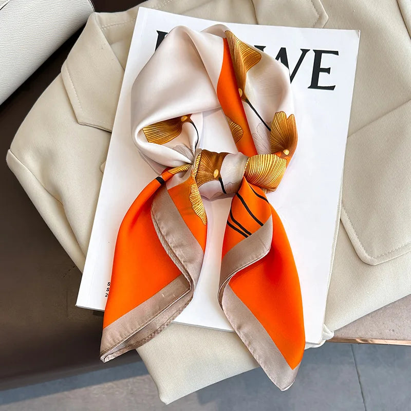 A luxury silk scarf in orange and beige tones tied into a bow, displayed on a white card.