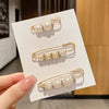 Gold-toned pearl brooch pins displayed on a white card against a blurred background.