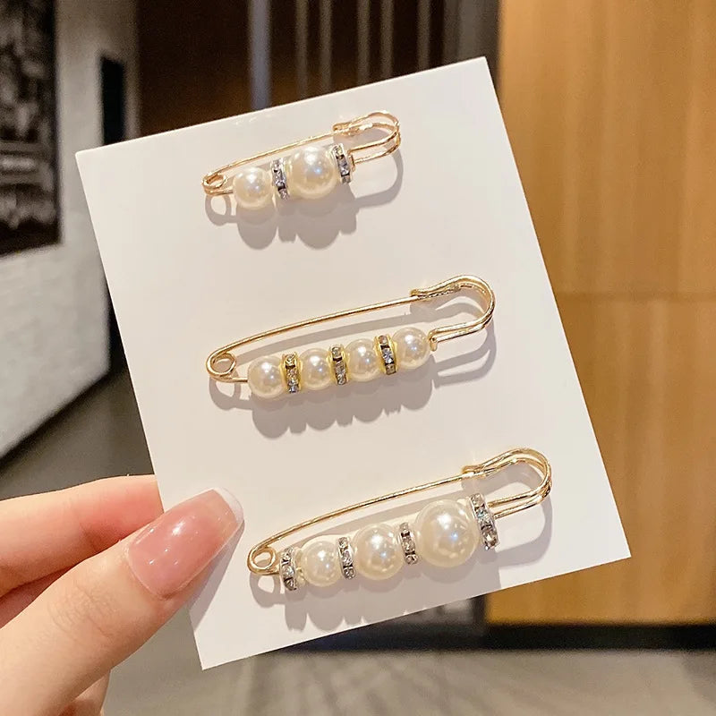Gold-toned pearl brooch pins displayed on a white card against a blurred background.