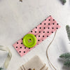 Pink polka dot fabric headband with a lime green button detail on a white background.