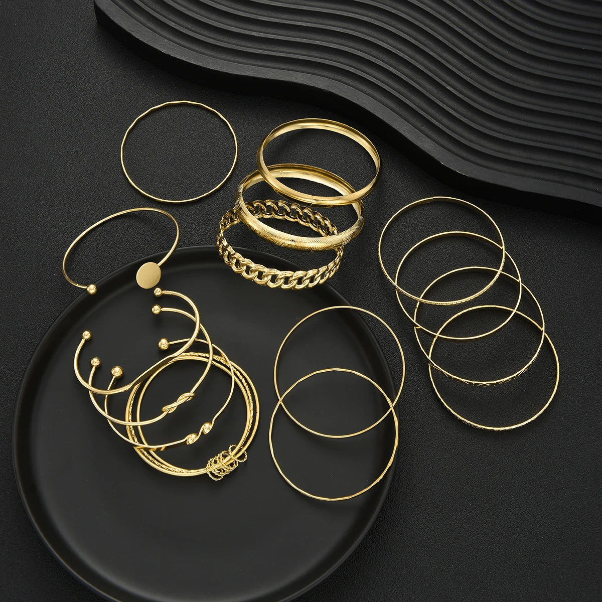 A set of gold geometric stackable minimalist bracelets arranged on a dark surface.