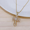 A dainty gold cross charm necklace with clear stones displayed on a white plate.