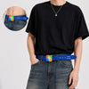 Una persona lleva un cinturón de computadora con estampado azul, diseño amarillo y verde, sobre jeans oscuros de mezclilla.