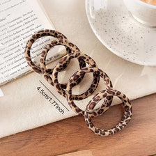 Un juego de gomas elásticas de pelo estampado de leopardo enrolladas en tela beige junto a un papel.