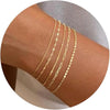 A stack of dainty gold plated bracelets worn on a wrist.