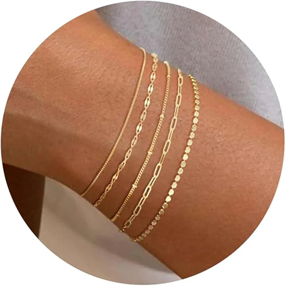A stack of dainty gold plated bracelets worn on a wrist.