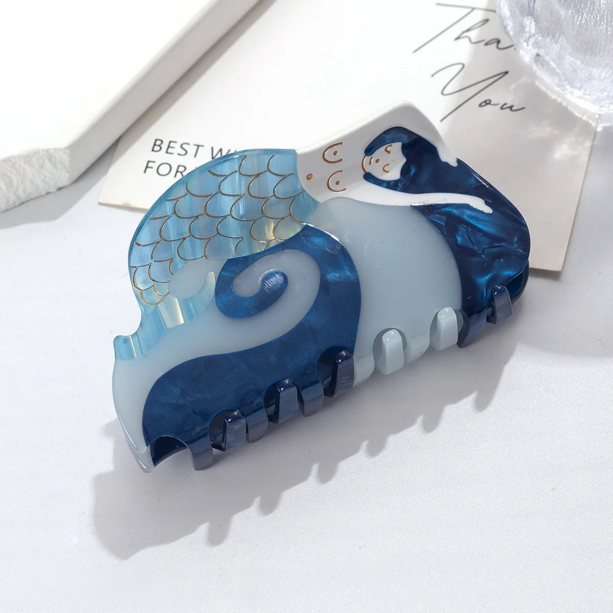 Pinza para el cabello de marfil azul y blanco con un diseño arremolinado y una pequeña cara.