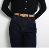A close-up of a brown leather belt worn over dark blue denim jeans and a black top.