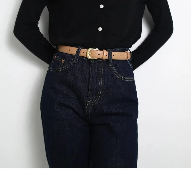 A close-up of a brown leather belt worn over dark blue denim jeans and a black top.
