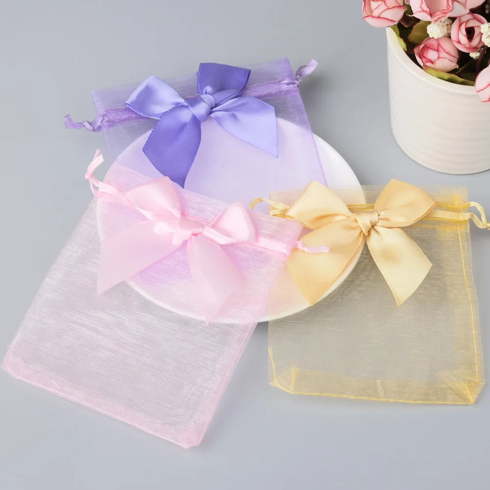 Three organza drawstring gift bags in purple, pink, and gold with satin ribbons