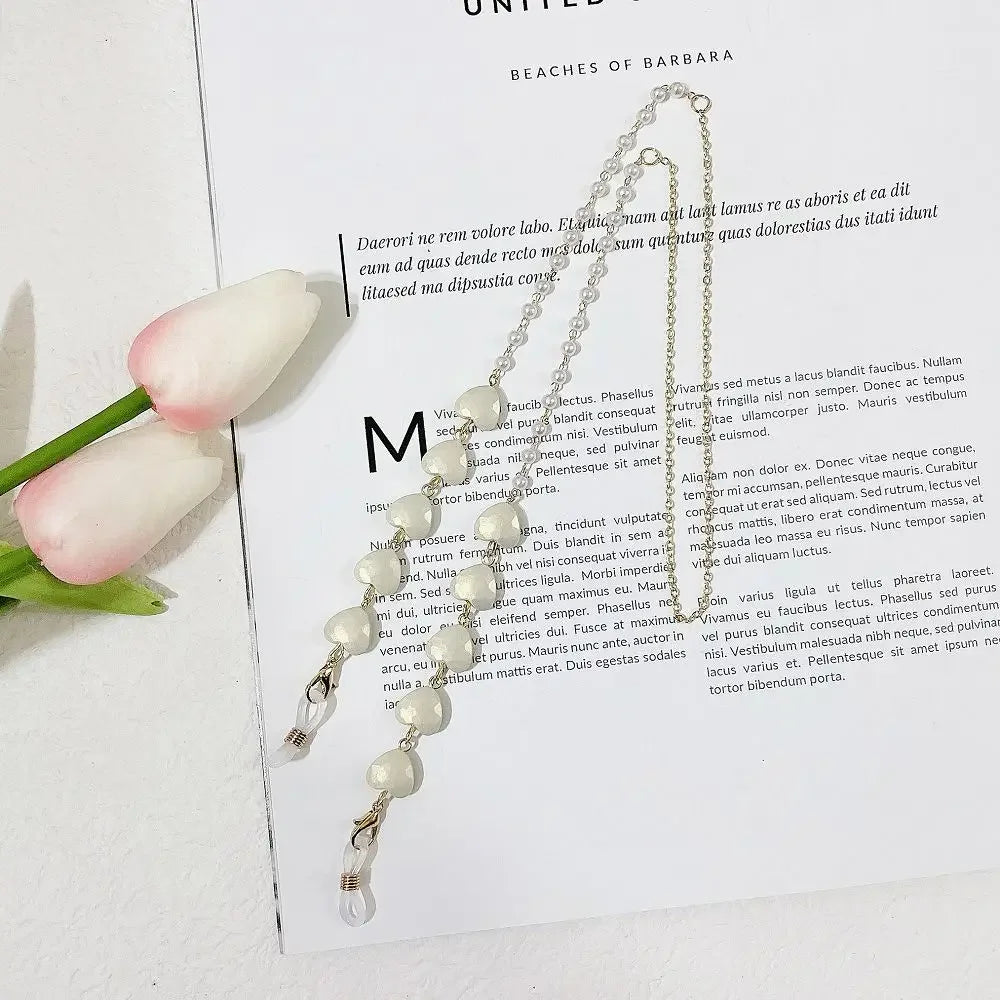 A delicate pearl beaded eyewear chain displayed next to a pink flower on a white background.
