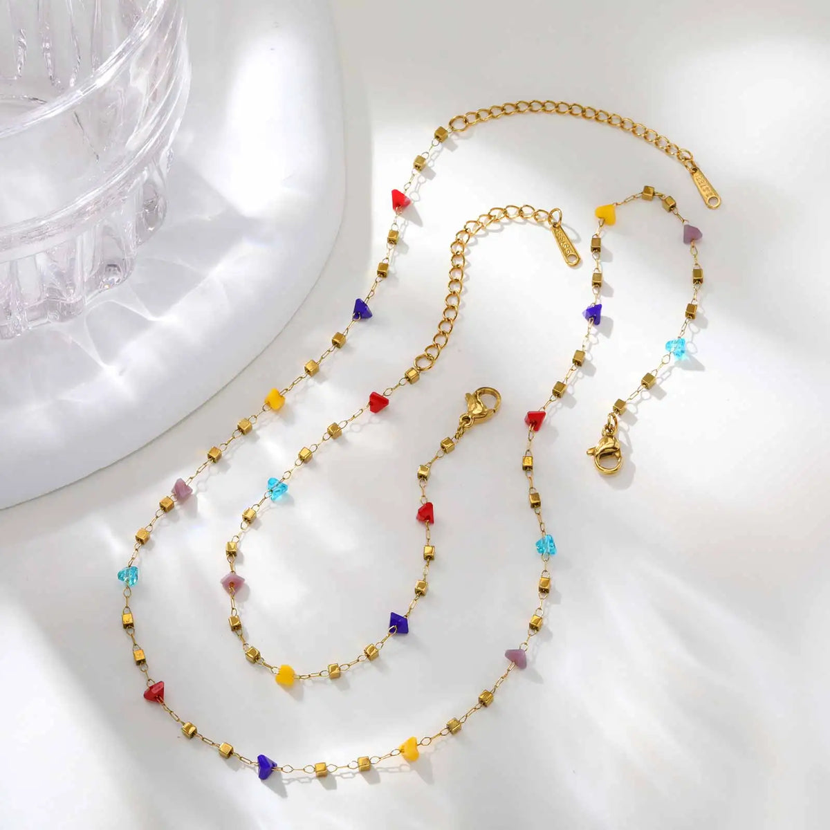 A gold chain necklace featuring irregular colored stones like red, yellow, blue, and purple.