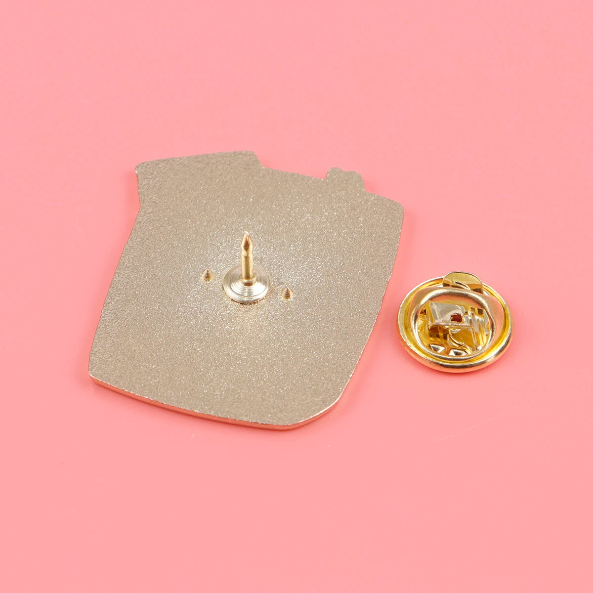 Broche poisson en émail couleur or avec son fond sur fond rose.