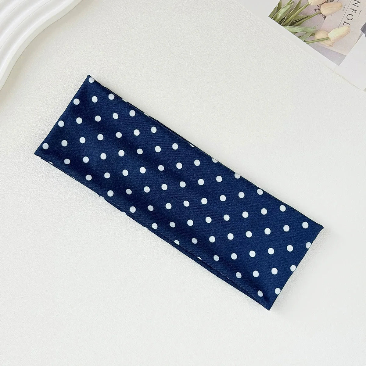 Navy blue fabric headband with white polka dots lying on a white surface.