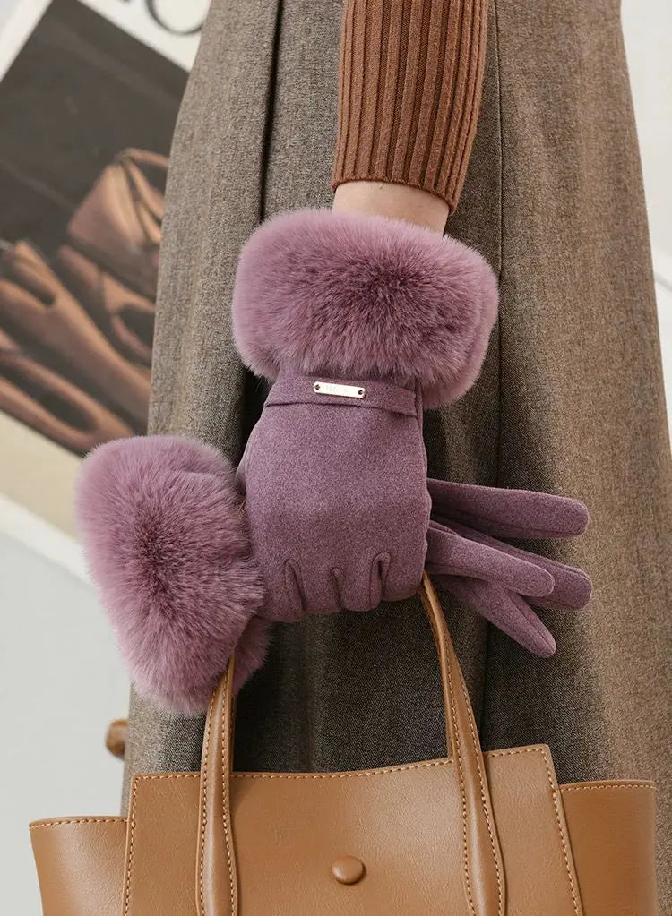 A close-up of a person wearing plush, mauve wrist gloves over a brown coat and holding a tan leather handbag.