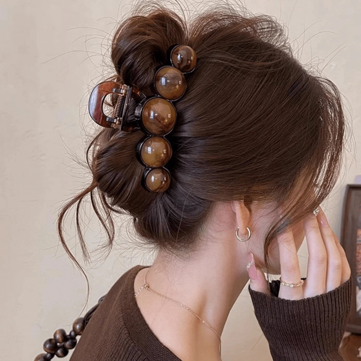 A woman's dark brown hair is styled in an elegant updo adorned with a decorative acrylic pearl hair claw clip.