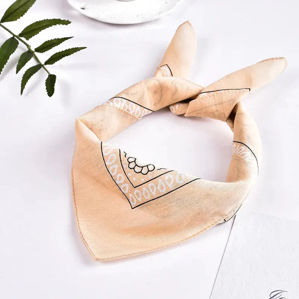 A beige bandana headband and wrist wrap set with black embroidered patterns on a white surface.