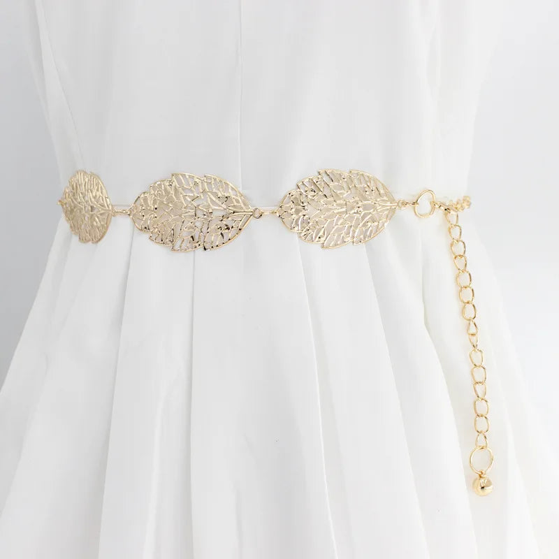 Cinturón de cadena de metal dorado con adornos en forma de hoja usado en un vestido blanco.