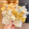 A hand holds a cluster of yellow and white fabric flower bow hair ties.
